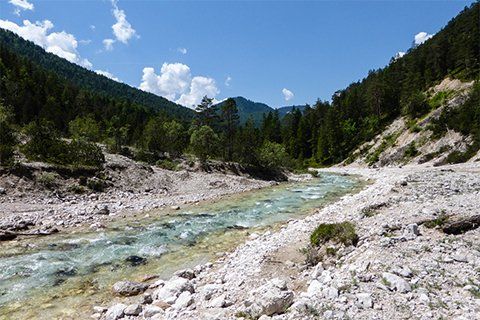 The Karwendel Höhenweg in Tirol offers breathtaking views of a river winding through a picturesque valley, set against the majestic backdrop of towering mountains.